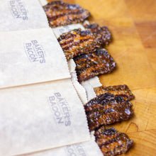 Load image into Gallery viewer, Baked bacon strips on a wooden surface with 'Baker's Bacon' packaging.